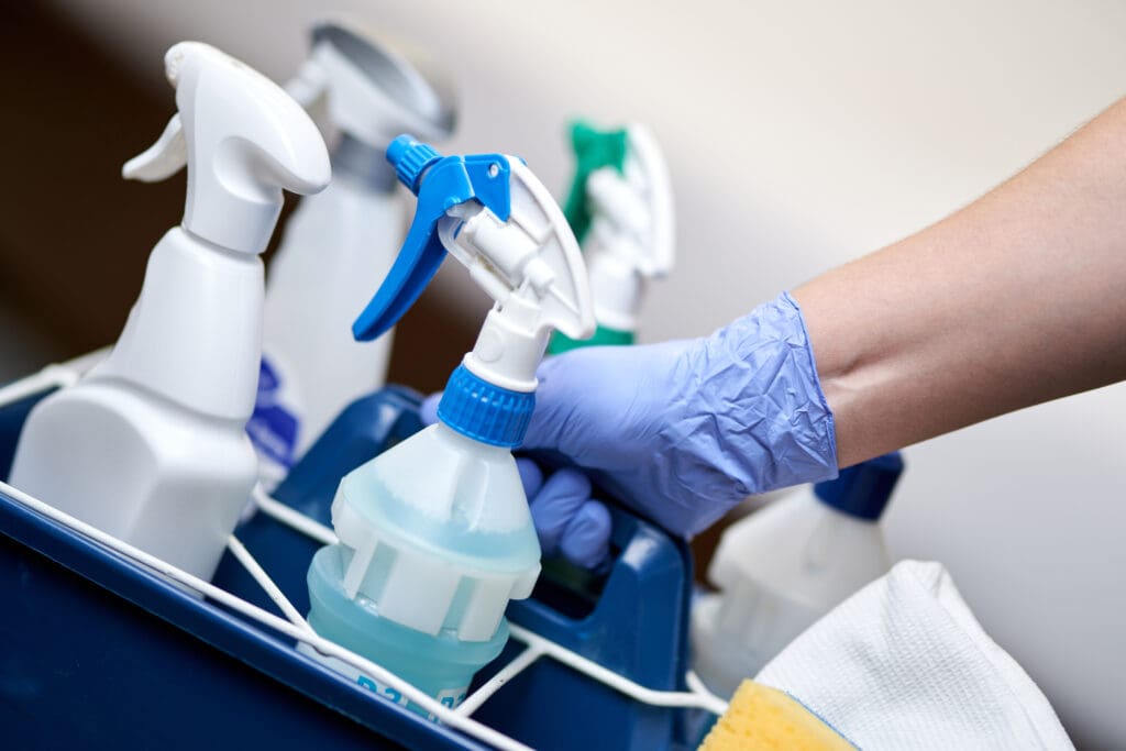Close up of a person holding a basket with cleaning supplies. 