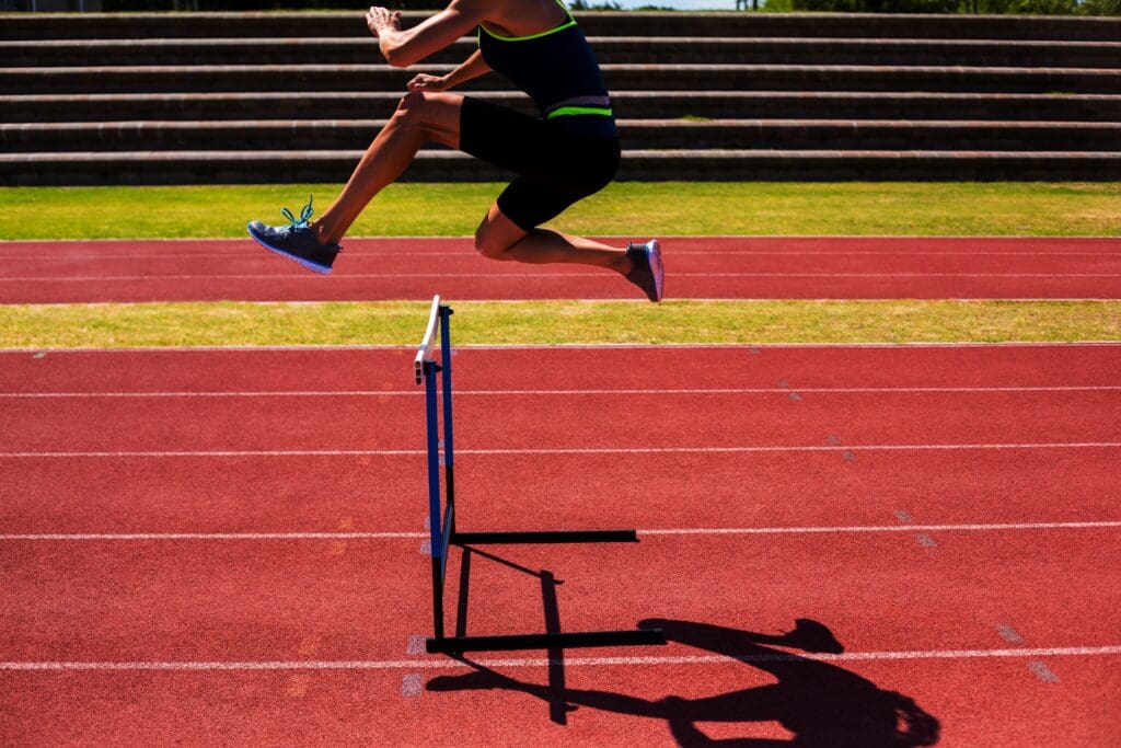 Female athlete jumping above the hurdle - Real-Estate-Leads